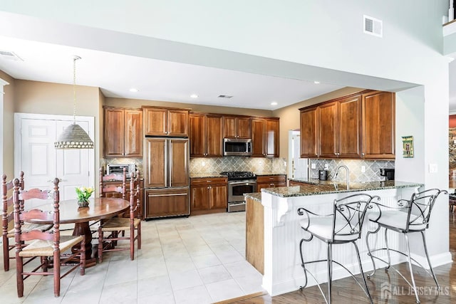 kitchen with visible vents, a breakfast bar area, dark stone countertops, a peninsula, and stainless steel appliances