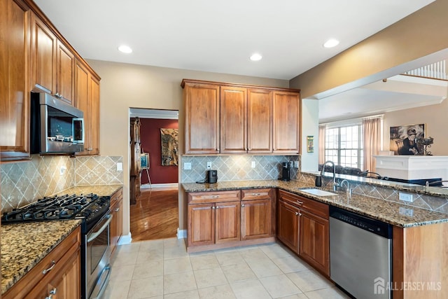 kitchen with appliances with stainless steel finishes, brown cabinets, a sink, and dark stone counters