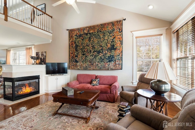 living area with lofted ceiling, ceiling fan, wood finished floors, and a multi sided fireplace