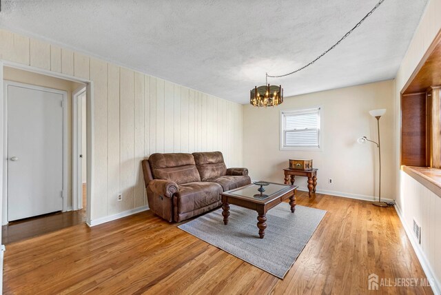 living room featuring light wood-type flooring, a textured ceiling, a chandelier, and wood walls