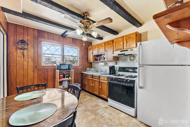 kitchen with ceiling fan, white refrigerator, gas range, beamed ceiling, and wood walls