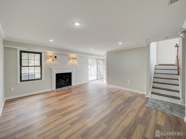 unfurnished living room with crown molding, visible vents, a fireplace with flush hearth, wood finished floors, and stairs