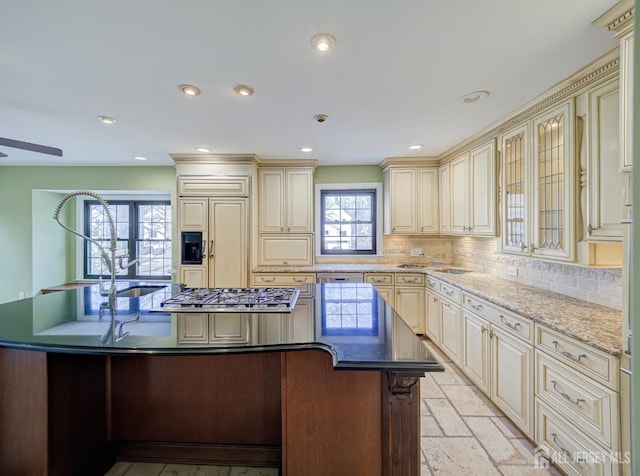 kitchen with paneled fridge, stainless steel gas cooktop, cream cabinetry, tasteful backsplash, and an island with sink