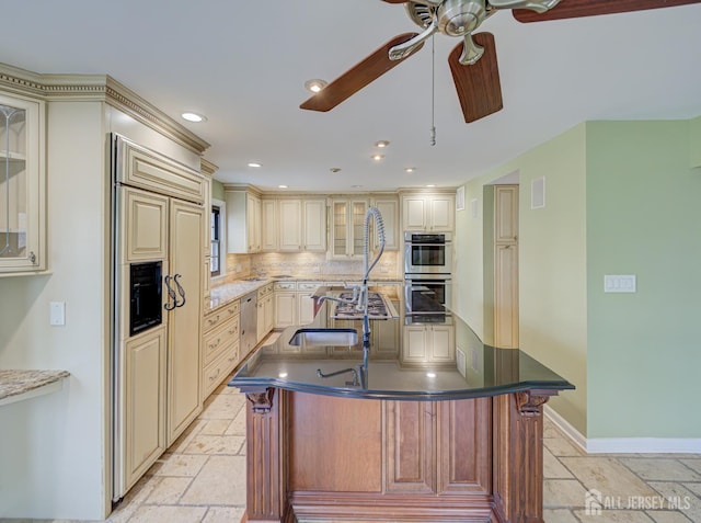 kitchen with cream cabinetry, stainless steel appliances, stone tile flooring, backsplash, and a kitchen island with sink