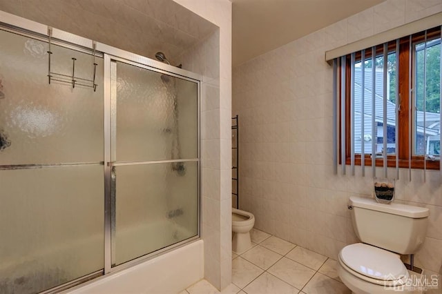 bathroom with tile patterned flooring, tile walls, toilet, and bath / shower combo with glass door