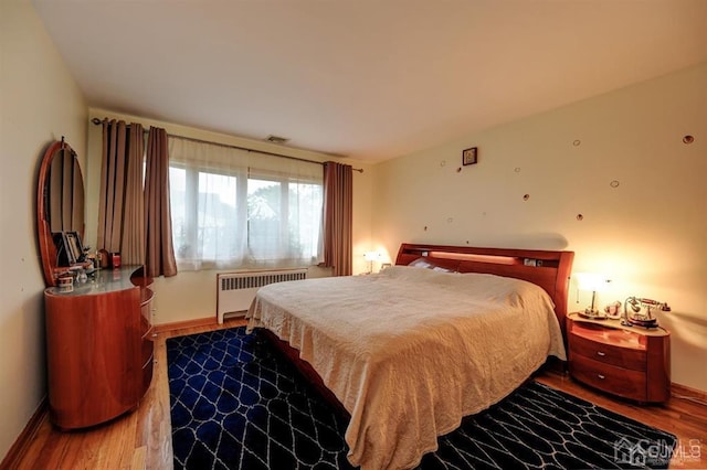 bedroom with radiator, baseboards, and wood finished floors