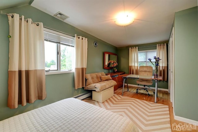 bedroom featuring multiple windows, wood finished floors, visible vents, and a baseboard radiator