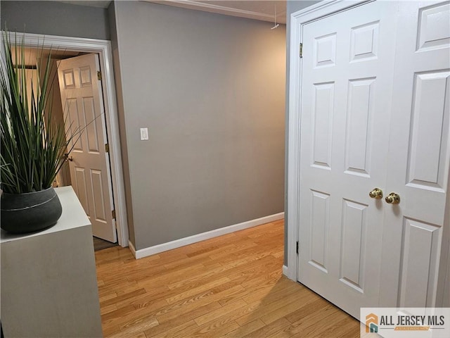 corridor with light wood-type flooring, attic access, and baseboards