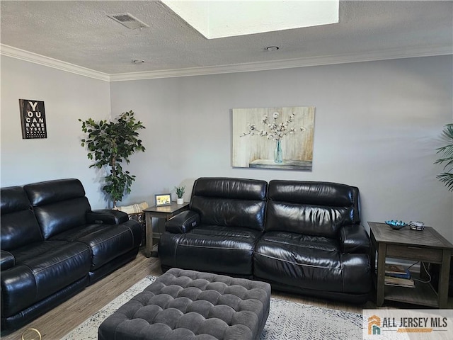 living area featuring a textured ceiling, ornamental molding, light wood-type flooring, and visible vents