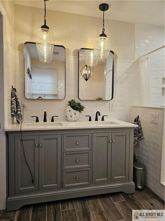 full bath featuring wood finish floors, a sink, tile walls, and double vanity