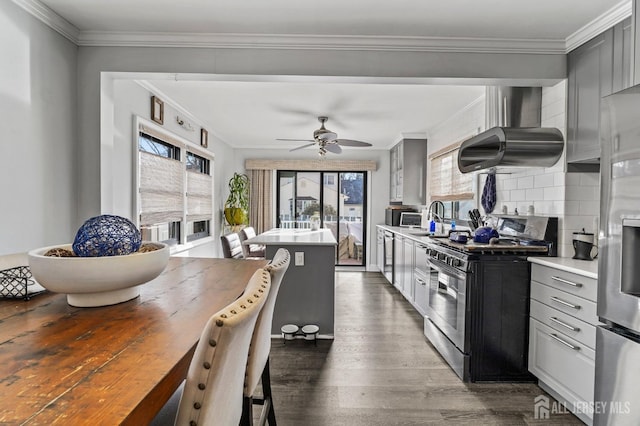 kitchen featuring appliances with stainless steel finishes, ornamental molding, wall chimney exhaust hood, and gray cabinetry