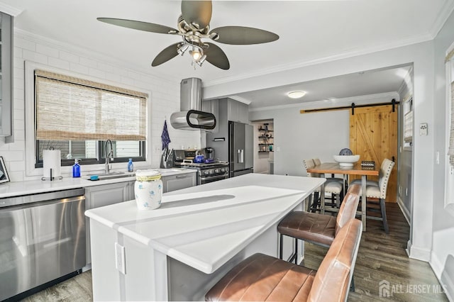 kitchen featuring gray cabinetry, dark hardwood / wood-style floors, stainless steel appliances, a barn door, and a breakfast bar area