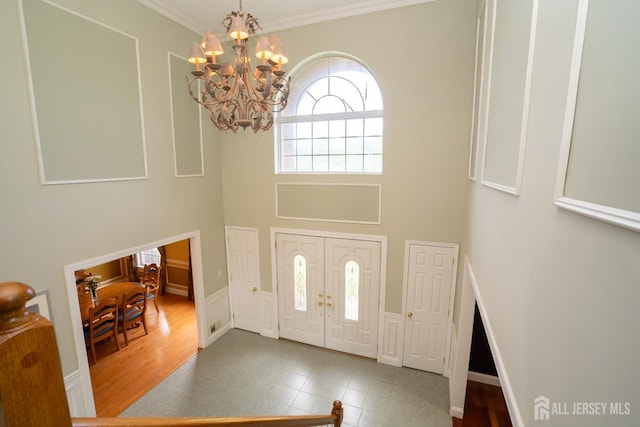 foyer entrance with a chandelier, crown molding, a towering ceiling, a decorative wall, and tile patterned flooring