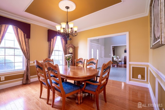 dining room with plenty of natural light, a chandelier, a tray ceiling, ornamental molding, and wainscoting