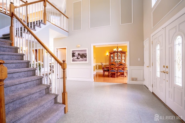foyer entrance with a towering ceiling, a decorative wall, stairway, a chandelier, and wainscoting