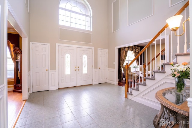 entryway with a decorative wall, stairway, a wainscoted wall, a towering ceiling, and light tile patterned floors