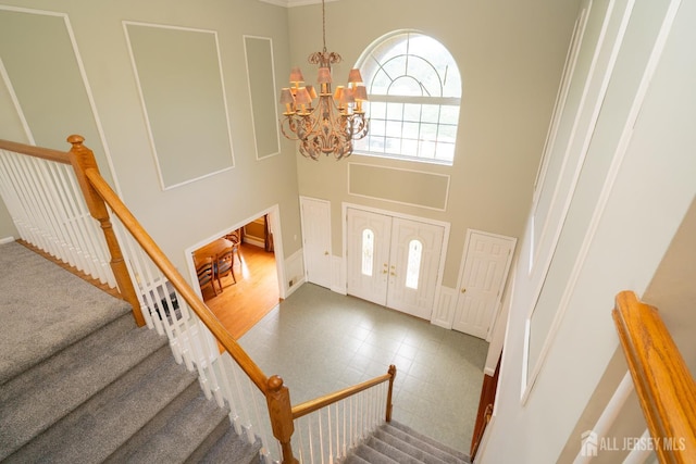 entrance foyer featuring a chandelier, a decorative wall, a towering ceiling, and stairs