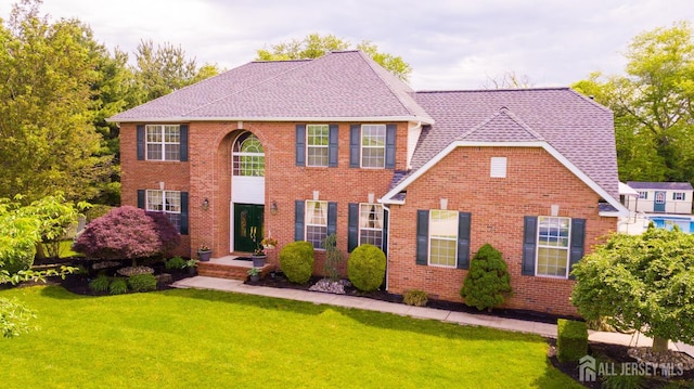view of front of home featuring a front yard, a shingled roof, and brick siding