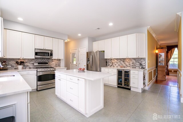 kitchen with stainless steel appliances, wine cooler, a kitchen island, decorative backsplash, and light countertops
