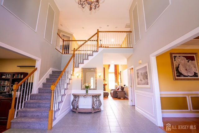 stairs with a high ceiling, tile patterned flooring, a decorative wall, a chandelier, and a wainscoted wall