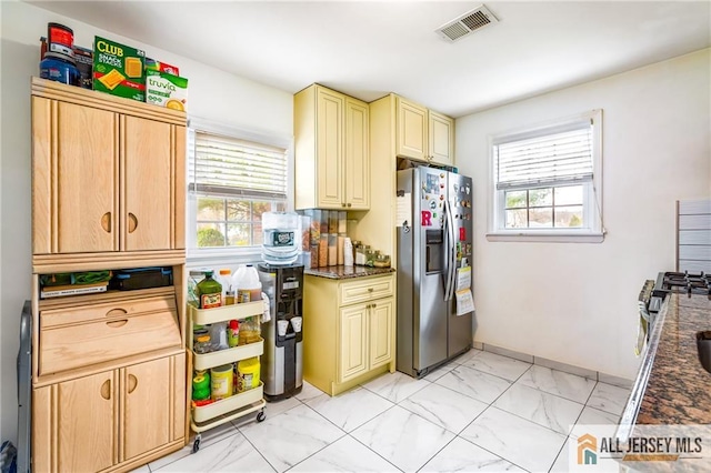 kitchen with stainless steel fridge, cream cabinetry, light marble finish floors, and healthy amount of natural light