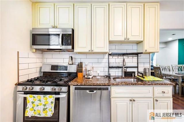 kitchen with stainless steel appliances, a sink, cream cabinetry, and decorative backsplash
