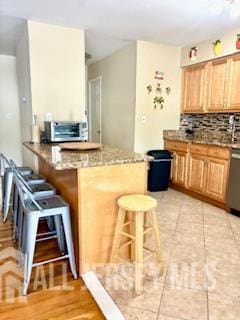 318 High St, Perth Amboy, NJ 08861 - kitchen featuring a breakfast bar, a peninsula, stainless steel dishwasher, decorative backsplash, and stone counters