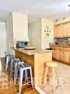 318 High St, Perth Amboy, NJ 08861 - kitchen with light brown cabinets, a breakfast bar, decorative backsplash, and stone countertops