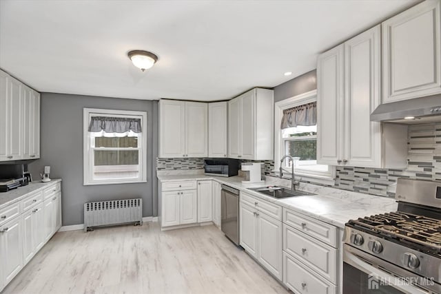 kitchen featuring radiator, under cabinet range hood, stainless steel appliances, white cabinetry, and a sink