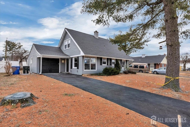 new england style home featuring a chimney, aphalt driveway, a shingled roof, and an attached garage
