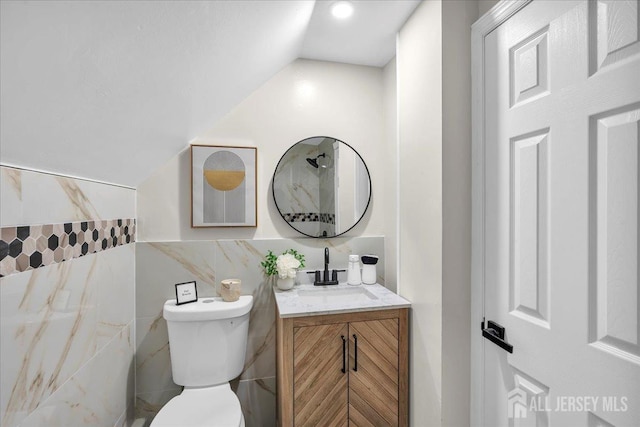 bathroom featuring lofted ceiling, vanity, toilet, and tile walls