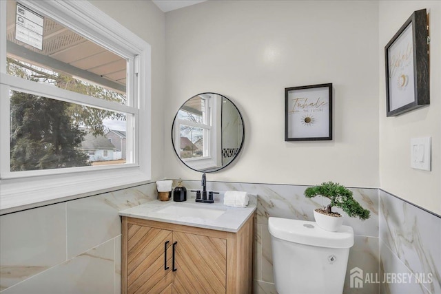 half bath with vanity, toilet, a wainscoted wall, and tile walls
