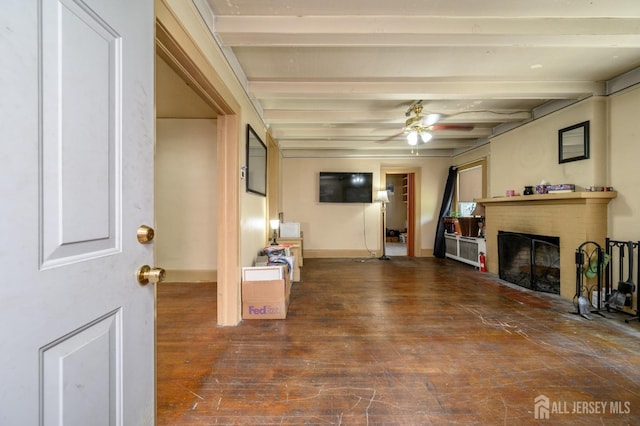 unfurnished living room with a brick fireplace, wood finished floors, beamed ceiling, baseboards, and ceiling fan