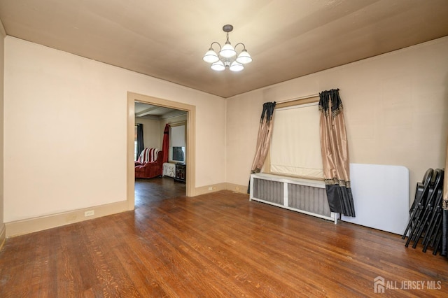 spare room with a chandelier, wood finished floors, and radiator