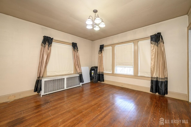 spare room with radiator, wood finished floors, and a chandelier