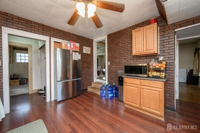 kitchen with dark countertops, appliances with stainless steel finishes, ceiling fan, brick wall, and dark wood-style floors