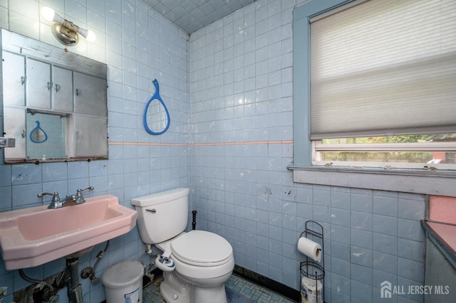 half bath with toilet, tile walls, and a sink