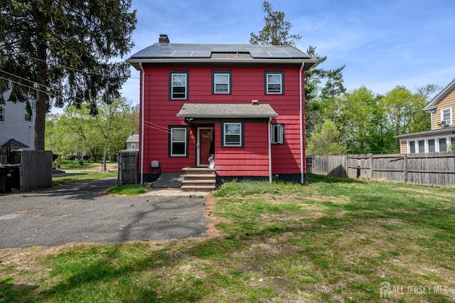 view of front of home featuring fence, solar panels, a front yard, and a chimney