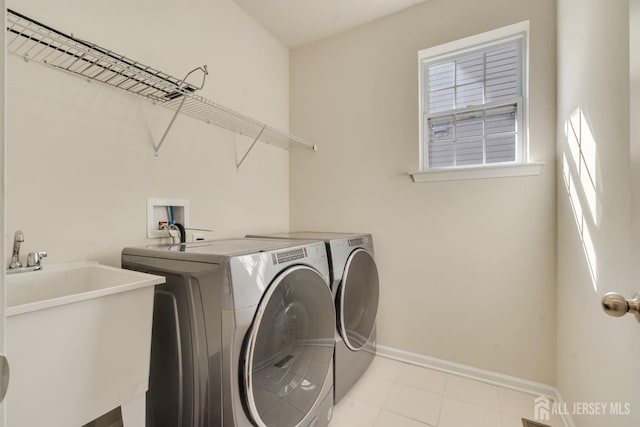 laundry area featuring laundry area, light tile patterned floors, baseboards, washing machine and clothes dryer, and a sink