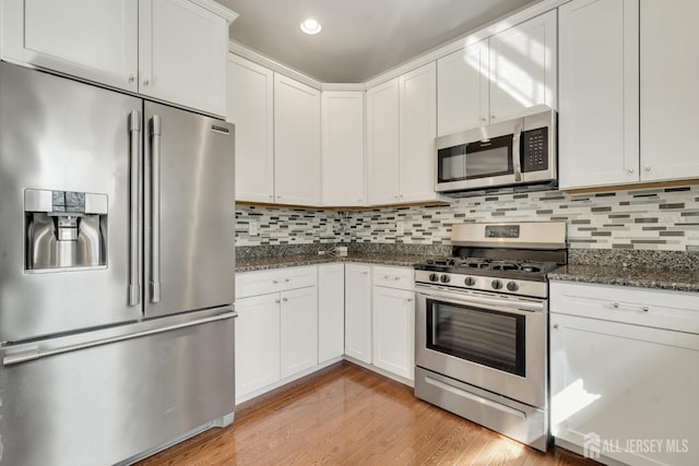 kitchen featuring white cabinets, appliances with stainless steel finishes, backsplash, dark stone counters, and light wood finished floors