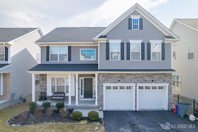 traditional-style house with stone siding, a porch, a shingled roof, and aphalt driveway