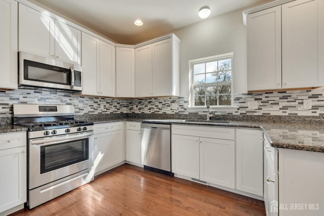 kitchen with stainless steel appliances, a sink, visible vents, decorative backsplash, and light wood finished floors