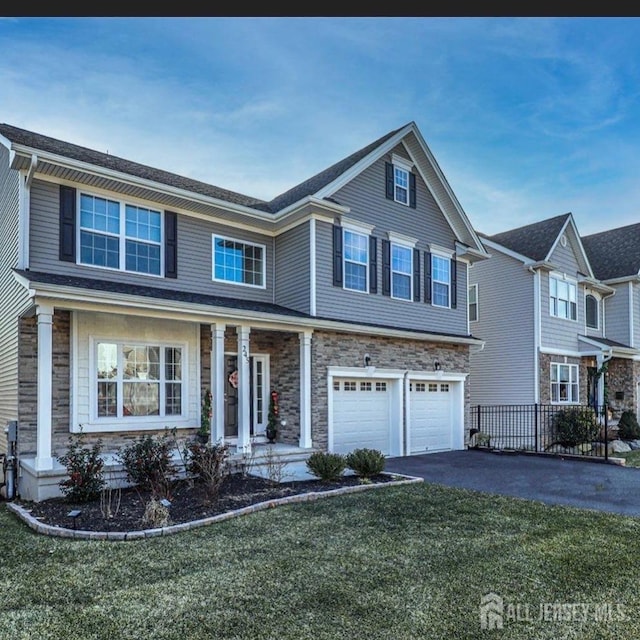 traditional home featuring a garage, a front yard, stone siding, and driveway