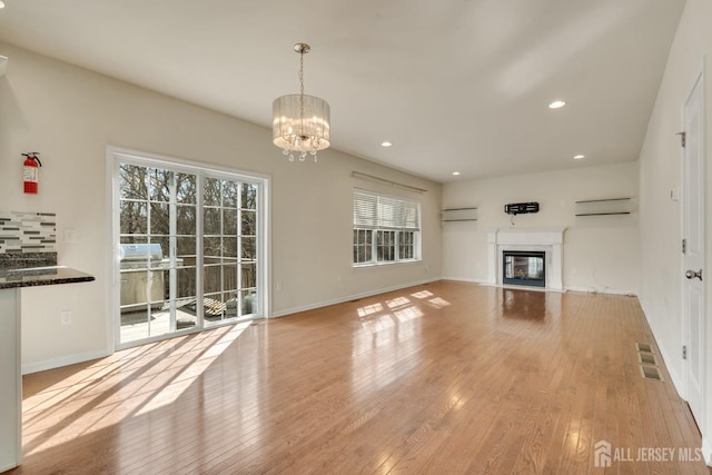 unfurnished living room with a fireplace with flush hearth, a wall mounted air conditioner, light wood-style floors, and visible vents