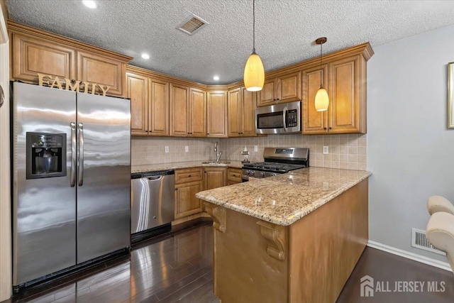 135 Hatfield Ln, East Brunswick, NJ 08816 - kitchen with light stone counters, appliances with stainless steel finishes, dark wood-style flooring, a peninsula, and brown cabinetry