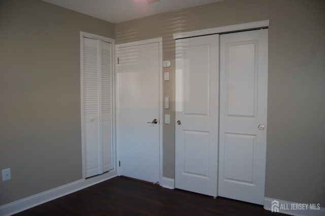 unfurnished bedroom featuring dark wood-style floors, two closets, and baseboards