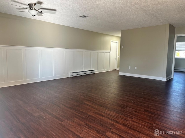 spare room with visible vents, a baseboard heating unit, ceiling fan, dark wood-style floors, and a decorative wall