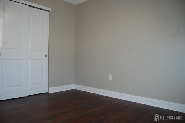 unfurnished bedroom with a closet, baseboards, and dark wood-style floors