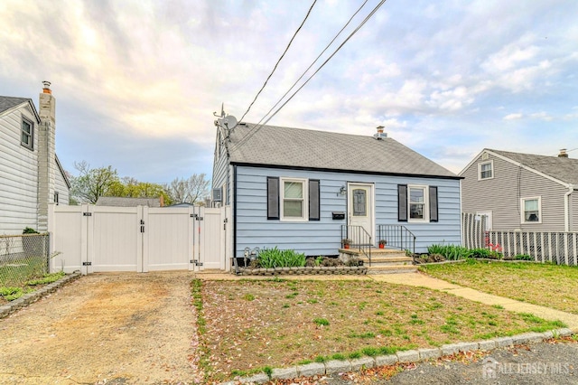 bungalow featuring a gate, fence, and roof with shingles