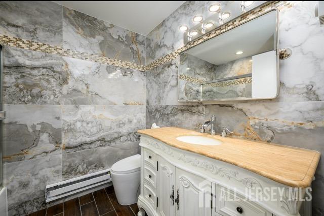 bathroom featuring wood finish floors, an enclosed shower, toilet, tile walls, and baseboard heating